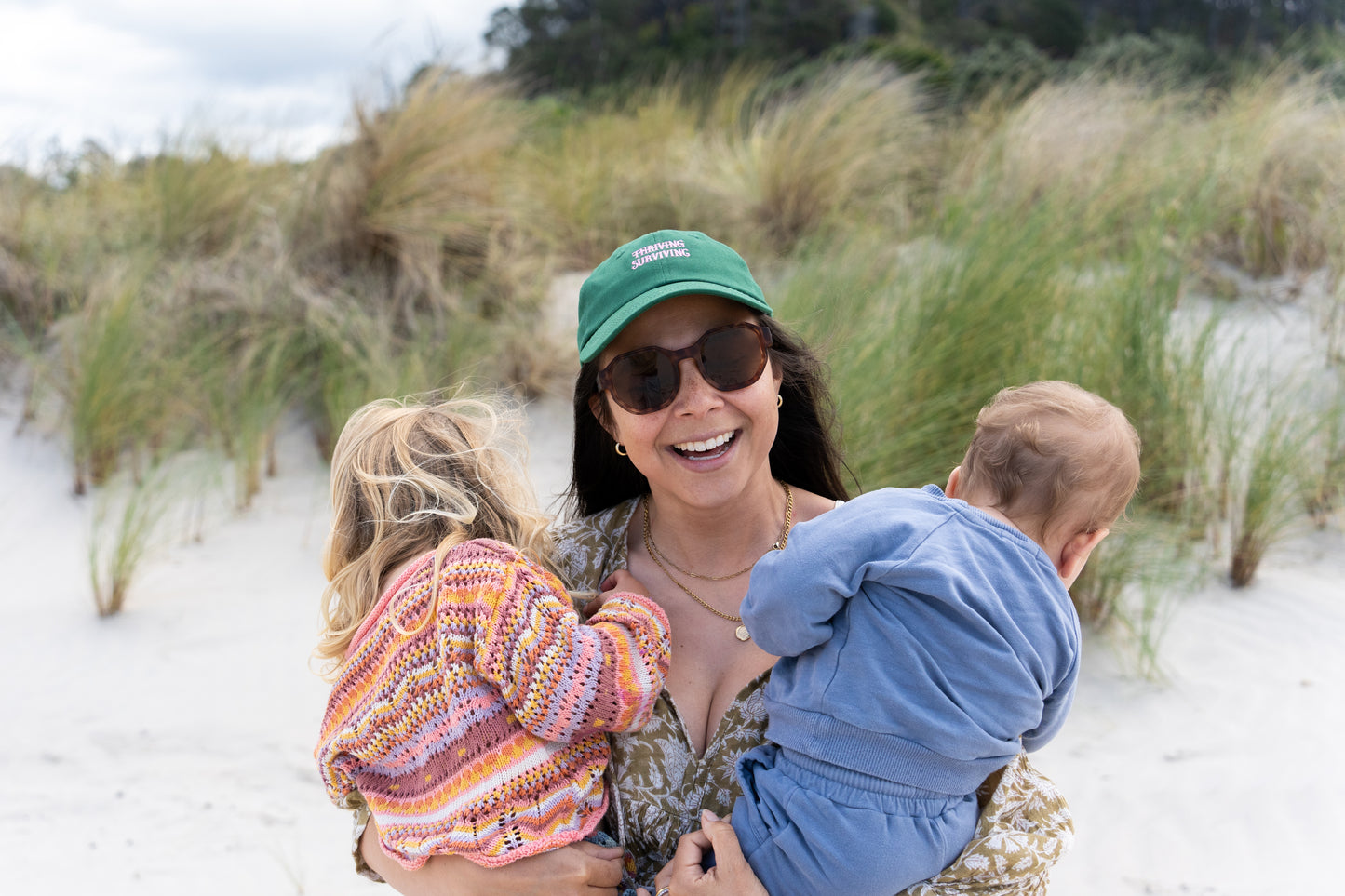 Stylish dark green adult hat featuring 'Thriving Surviving' text, a great accessory for busy parents.